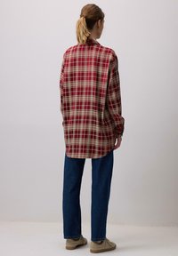 Punane ja kreemjas ruudulises mustris oversize-särk pika varrukaga, �ümarate servadega, koos siniste sirgete pükste ja beežide kingadega.