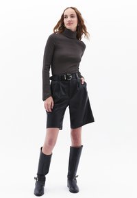 Bruine lange mouw turtleneck, zwarte geplisseerde shorts, zwarte hoge hakken met gespen, zachte texturen, minimalistisch ontwerp, neutrale kleuren.