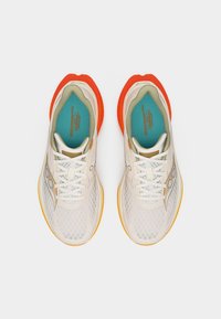 Ζεύγος λευκών αθλητικών παπουτσιών από δίχτυ με πορτοκαλί σόλες και τιρκουάζ πάτους, φωτογραφημένα από πάνω σε λευκό φόντο.