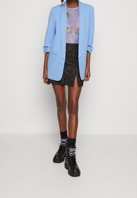 Person wearing a light blue blazer over a printed purple top, black textured mini skirt with front slit, black socks, and black platform boots.