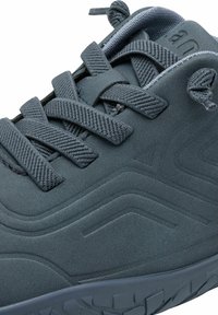 Dark gray sneaker close-up showing textured synthetic upper, thick woven laces, padded tongue, and rugged sole pattern.