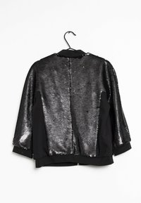 Czarna kurtka z cekinowym tyłem i czarnymi rękawami z materiału. Posiada okrągły kołnierz, zamek błyskawiczny i luźny krój.