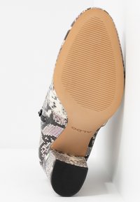 Flerfärgad högklackad sko med ett texturerat orm-skinnmönster. Brun gummisula med grepp, märkt "ALDO" nära hälen.