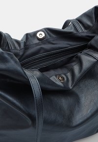 Borsa tote in pelle nera con una texture morbida, forma morbida, tasca interna con zip e chiusura a scatto in metallo argentato. Presenta manici lunghi.