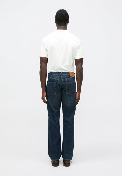 Sinised teksapüksid sirge lõikega, millel on vöökohal pruun nahkne plaastritükk ja tagataskutel peened õmblused.