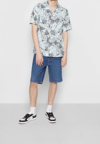 Camicia azzurro chiaro a maniche corte con stampa di foglie e fiori neri, abbinata a pantaloncini di denim e sneakers bianche e nere.