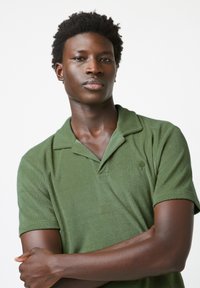 Groene poloshirt van een zachte, gestructureerde stof, met een kraag, korte mouwen en een klein boomlogo op de linkerkant van de borst.
