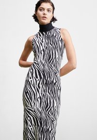 Abito senza maniche con collo alto, caratterizzato da un motivo a strisce zebra bianco e nero. Realizzato in tessuto morbido con una silhouette aderente.