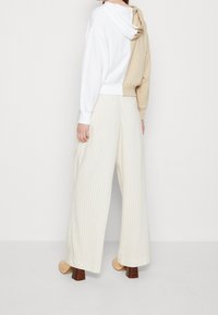 Felpa bicolore bianca e beige, vestibilità ampia, abbinata a pantaloni a palazzo a righe color crema. Scarpe con tacco color beige chiaro completano l'outfit.