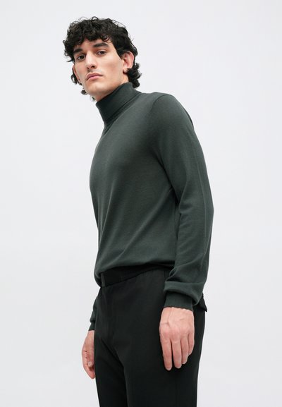 Temnozelena turtleneck pulover iz mehkega materiala, oprijetega kroja z dolgimi rokavi, v kombinaciji z črnimi hlačami. Minimalističen dizajn, gladka tekstura.