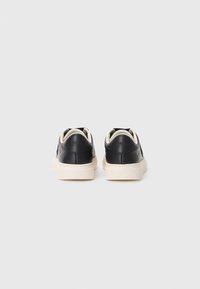 Sorte lærersneakers med en hvit såle og kontrasterende hælaksenter, minimalistisk design med preget merkevarebakgrunn.