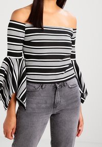 Top scollato con righe orizzontali bianche e nere, con ampie maniche a campana. Abbinato a jeans grigi a vita alta.