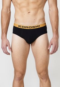 Schwarze Herrenbriefs aus Baumwolle mit einem gelben KOROSHI-Logo-Bund. Verfügt über einen klassischen Schnitt und eine gestickte Detail vorne.