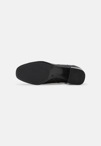 Suela de zapato negra con un acabado de goma suave, que presenta una superficie texturizada para mayor agarre y una etiqueta que indica "ANTI-DESLIZANTE" en texto en relieve.