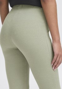 Csíkos, világoszöld leggings, magas derékkal. Feszes kivágása és sima tapintása van, amely letisztult dizájnt mutat, látható minták nélkül.