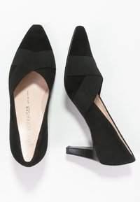 Tacchi alti in suede nero con punta affusolata, dotati di fasce elastiche incrociate. Il tacco è di tipo impilato per un tocco di ulteriore dettaglio.