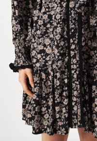 Abito floreale con sfondo blu navy e fiori beige, maniche a sbuffo e bordo e polsini in pizzo nero. Stile comodo.