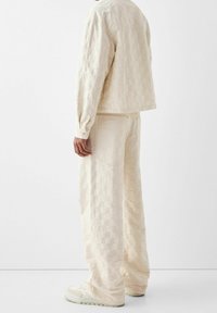 Ljusbeige strukturerad jacka och matchande byxor med rutmönster. Bärs med ljusa sneakers, visad bakifrån.