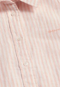 Leichtes, gestreiftes Hemd in Pfirsich und Weiß mit kleinen runden Knöpfen, weichem Stoff und gesticktem Logo auf dem Gewebe.