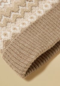 Beżowy sweter z wełny z wzorem oraz teksturowanym, prążkowanym mankietem. Górna część ma jasnokrémowy geometryczny wzór na miękkim beżowym tle.