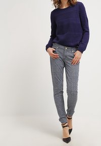 Suéter navy con rayas horizontales texturizadas, combinado con pantalones slim-fit de patrón en blanco y azul, y tacones negros de punta.