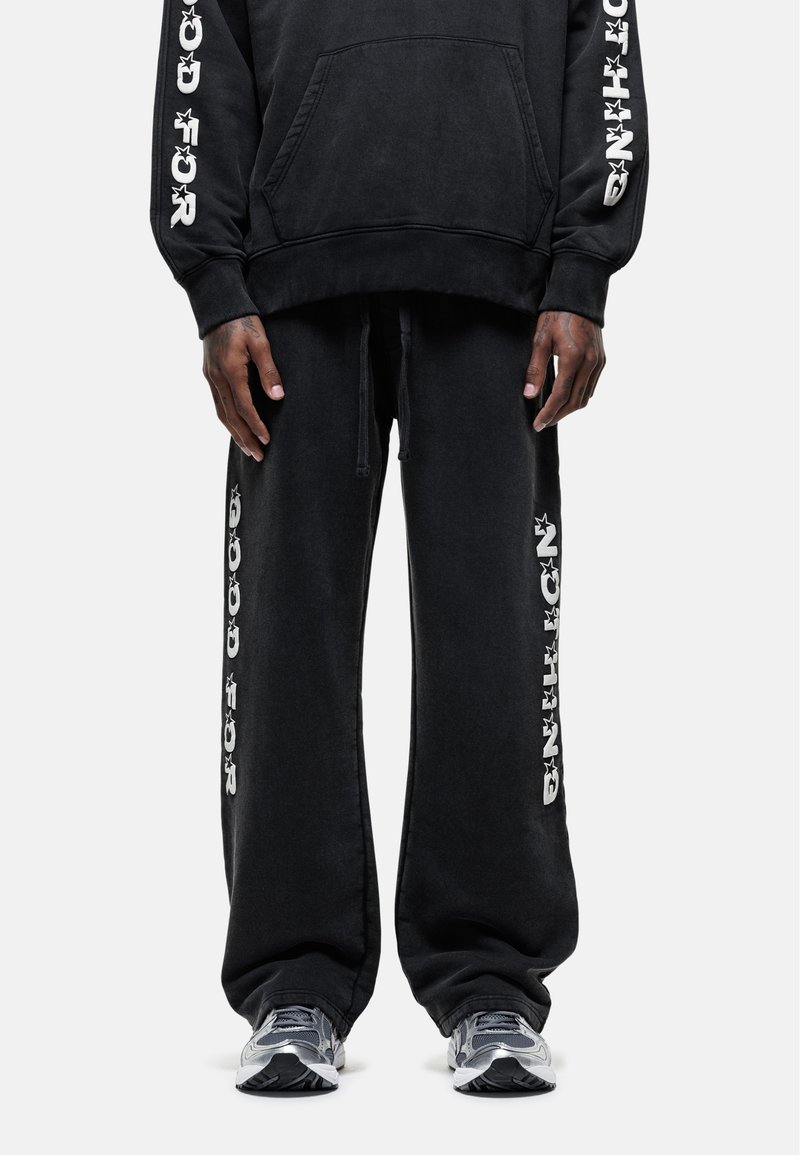 Zwarte katoenen hoodie met een voorzak en witte grafische tekst op de mouwen, gecombineerd met bijpassende zwarte joggingbroek in een losse pasvorm met zijprints.