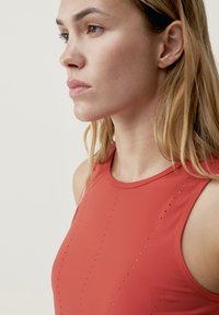 Červený atletický tielko s okrúhlym výstrihom, so perforovanými detailmi na prednej strane pre ventiláciu. Hladká textúra, bezrukávový dizajn.