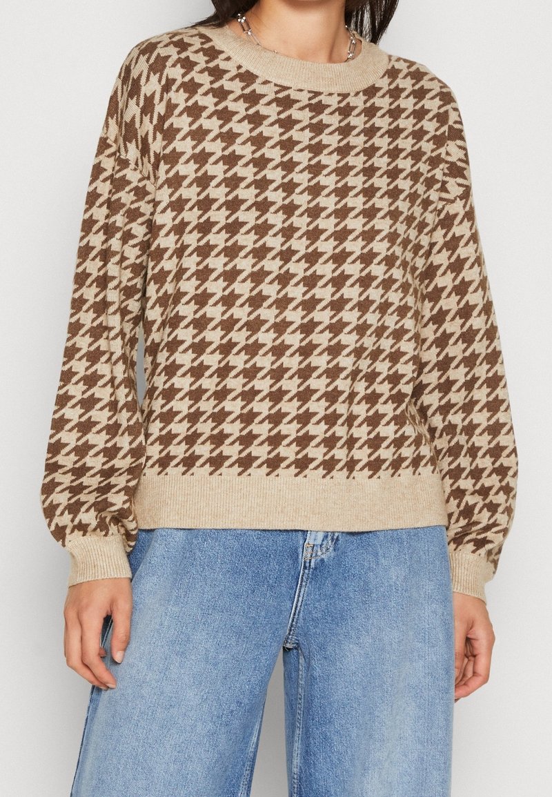 Brun och beige hounds-tooth-mönstrad stickad tröja med rund halsringning och ballongärmar, tillsammans med blå jeans.