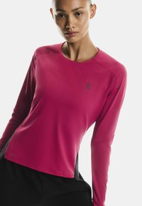 Majica dugih rukava za sport u živopisnoj ružičastoj boji, rebraste teksture, s crnim bočnim panelom i malim crnim logotipom na grudima.