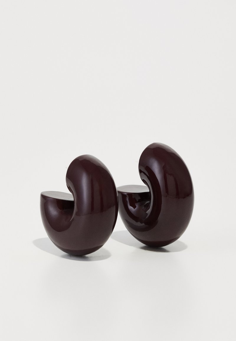 Gekrümmte Skulpturen in tiefem Burgunderrot mit glänzender Oberfläche, die Halbkreis-Ausschnitte und eine glatte Textur aufweisen und abstrakten Schneckenformen ähneln.