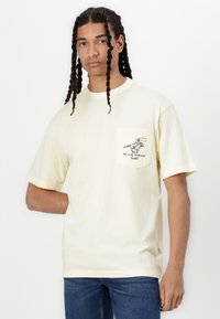 T-shirt en coton jaune clair à manches courtes, avec une poche poitrine et un graphique d'un cowboy avec le texte "PAS DE FUITES".