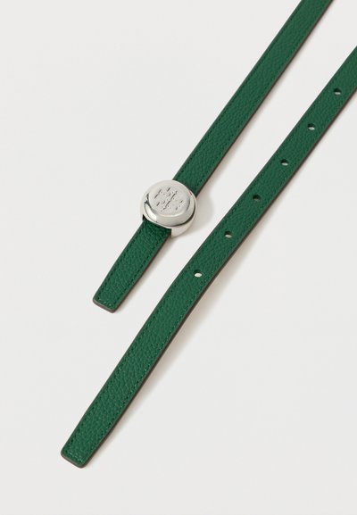 Πράσινη υφασμένη δερμάτινη ζώνη με στρογγυλή ασημένια πόρπη που διαθέτει ανάγλυφο σχέδιο σε σχήμα σταυρού, ξαπλωμένη σε λευκό φόντο.