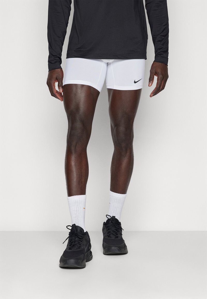 Vita sportshorts med en svart Nike-logga, kombinerat med svarta sneakers, vita strumpor och en svart långärmad skjorta.