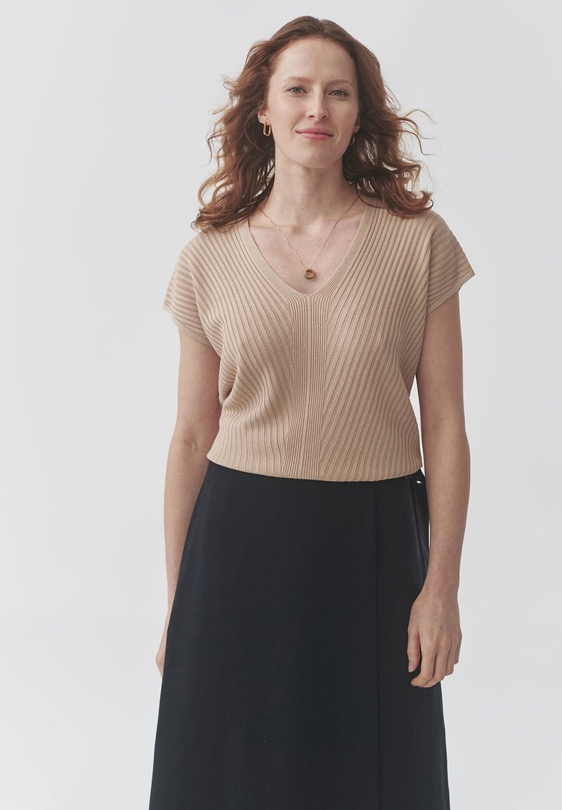 Top de punto acanalado Beige de manga corta con diseño de cuello en V, combinado con una falda negra. Construcción sencilla, textura suave.