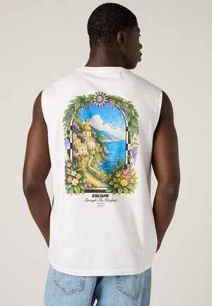 Homme portant un débardeur blanc avec un imprimé coloré de village côtier et d'océan encadré de fleurs et de feuilles, le texte indique « Escape Through The Window. »