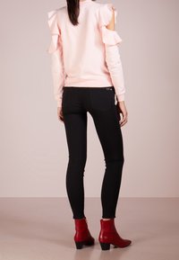 Sudadera rosa claro con mangas con volantes, combinada con vaqueros pitillo negros y botines rojos con tacón bajo y detalles dorados.