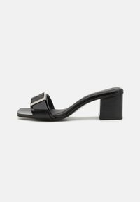 Mules à talons noirs avec une finition laquée brillante, détail de boucle carrée, design ouvert à l'avant et un talon bloc moyen pour plus de stabilité.