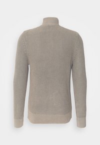 Beige stickad tröja med hög krage, ribbat mönster och långa ärmar. Längden är något svängd och har en åtsittande manschett.