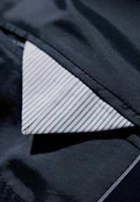 Granatowy materiał o gładkiej teksturze, z złożonym kołnierzem, który odsłania wzór białych pasków poniżej, o sztywnych i starannie przeszytych krawędziach.