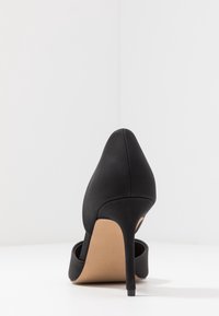 Décolleté nera con finitura in satin lucido, punta affusolata e tacco a stiletto sottile. Presenta un accento testurizzato nero nella parte anteriore.