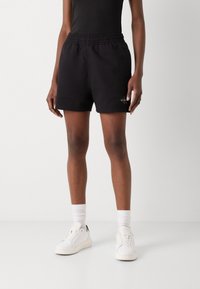 Svarta bomullsshorts med elastisk midja, prydda med en liten logodetalj, i kombination med vita sneakers och ribbad vita strumpor.
