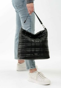 Black quilted handbag with a soft texture, featuring a shoulder strap, silver hardware, and a subtle brand logo on the front.