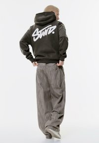 Felpa con cappuccio grigio scuro con un grande logo bianco sulla schiena. Abbinata a pantaloni a gamba larga grigio chiaro a righe e sneakers bianche.
