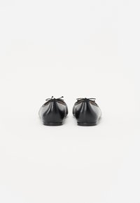 Bailarinas de cuero negro con punteras redondeadas, acabado texturizado y pequeños lazos decorativos en la parte trasera, que cuentan con una suela baja y plana.