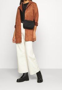 Brun ruskinds overskjorte, sort crossover taske, sorte combat støvler og off-white brede bukser. Teksturerede stoffer med kontrastfarver.