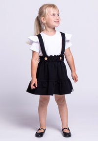 Czarna bawełniana sukienka z regulowanymi ramiączkami, marszczonym elastycznym pasem i warstwowym dołem z falbanami. Połączona z białą koszulą z krótkim rękawem i czarnymi butami.