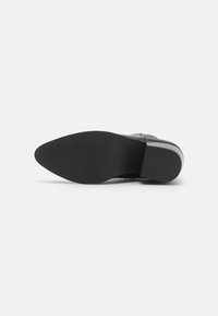 Suola di scarpa nera con forma appuntita. Presenta un gomma testurizzata per una buona aderenza, design piatto e una leggera curvatura nel tallone.
