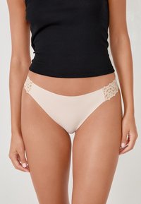 Completini in pizzo color nudo con un tessuto morbido e liscio, design a vita bassa e un delicato motivo floreale sulla vita.