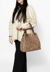 Borsa in pelle marrone con motivo floreale a rilievo e doppio manico corto. Realizzata in materiale durevole, presenta motivi intricati e una forma leggermente strutturata.