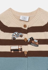 Cardigan en maille avec des rayures beige, marron et bleue. Il dispose de boutons et de véhicules brodés : une voiture, un camion et des engins de construction.